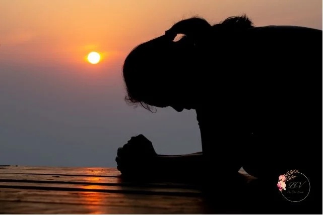 Silhouette of a person kneeling at sunset near the water, symbolizing surrender, prayer, and emotional stillness