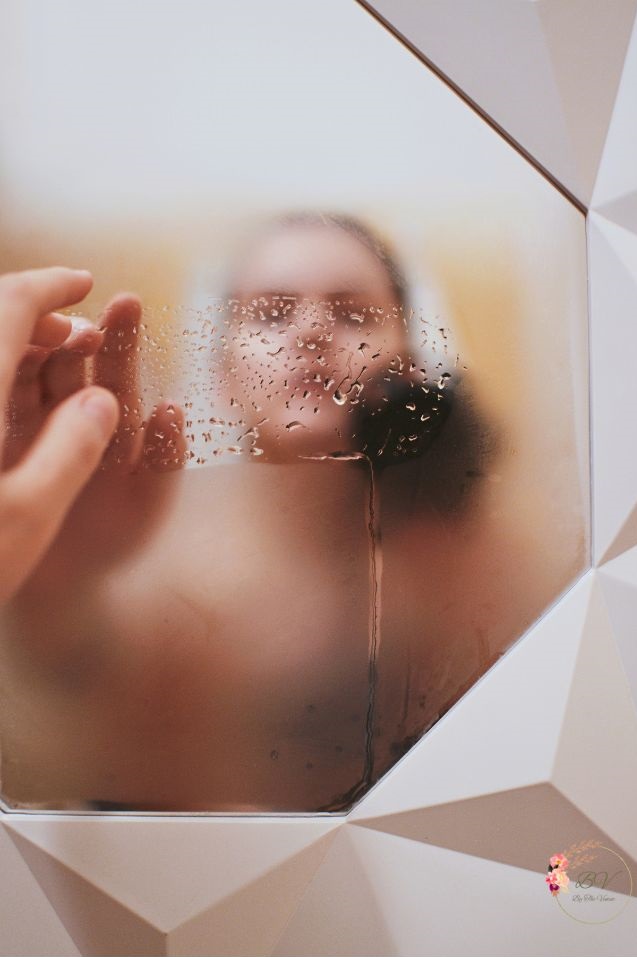 A blurred woman's reflection through a foggy mirror as she touches the glass- symbolic of invisible signs of hashimoto